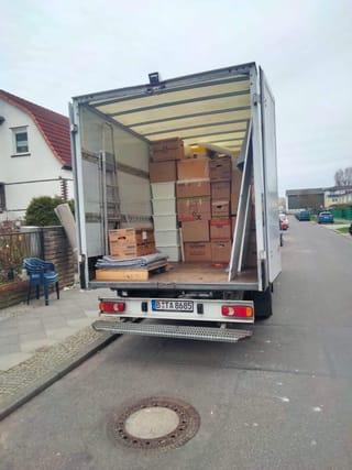 Beladener Umzugswagen mit gestapelten Umzugskartons und Transportdecken vor einem Wohnhaus