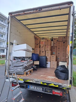 Voll beladener Umzugswagen mit Umzugskartons, Matratzen und gestapelten Transportdecken