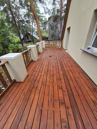 Neu verlegte Holzterrasse mit rotbraun lasierten Dielen entlang einer Hauswand