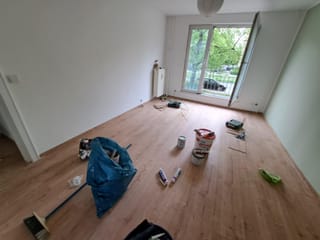 Leerer Wohnraum während der Renovierung mit Farbeimern, Werkzeug und frisch gestrichenen Wänden
