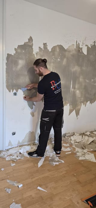 Mitarbeiter von Berlin Umzüge entfernt alte Tapete mit einem Spachtel von der Wand